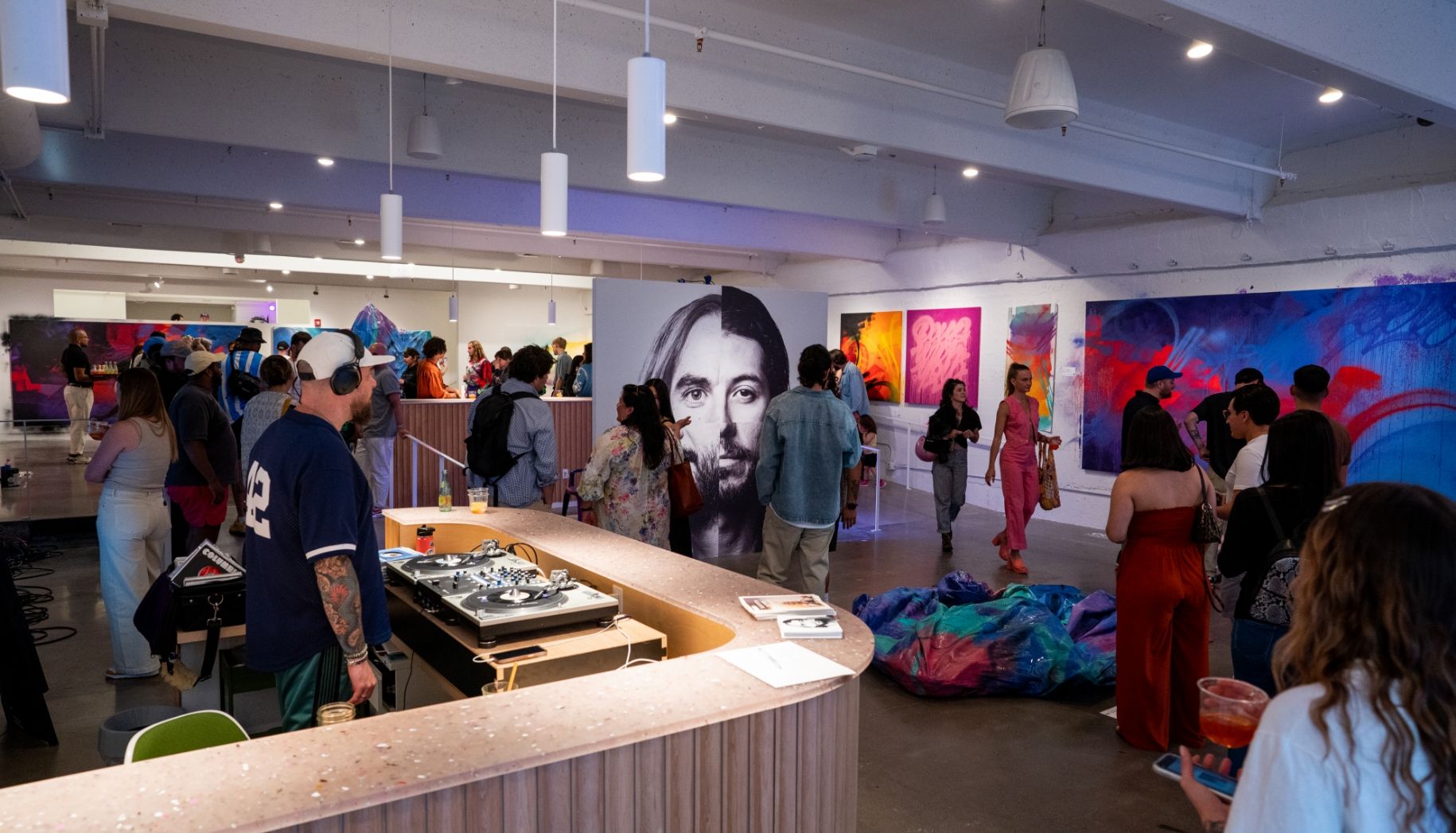 View of Gallery during opening party from entrance corner. DJ and dozens of people drinking and socializing amongst paintings and sculptures