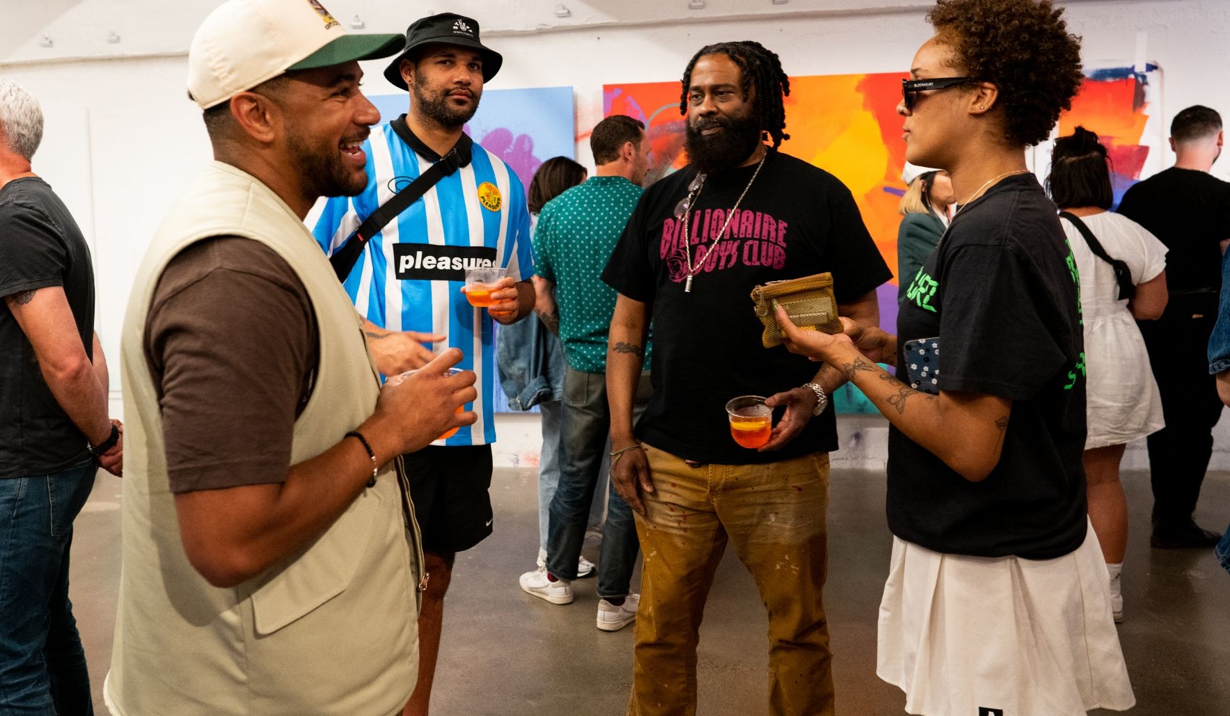 several exhibit attendees socialize in front of large colorful paintings