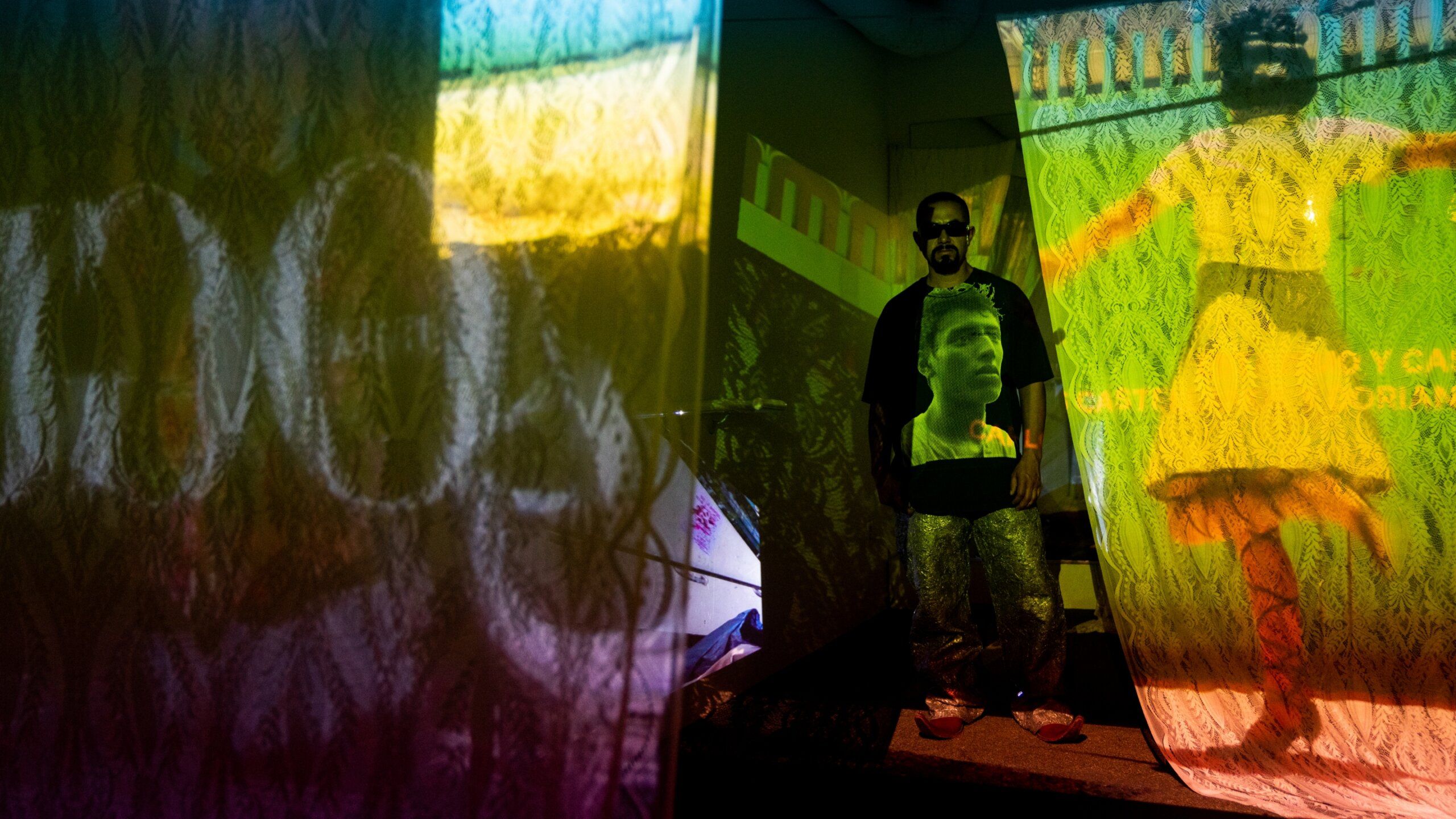 Dorian stands in room with multiple projections of his video work onto sheer fabric