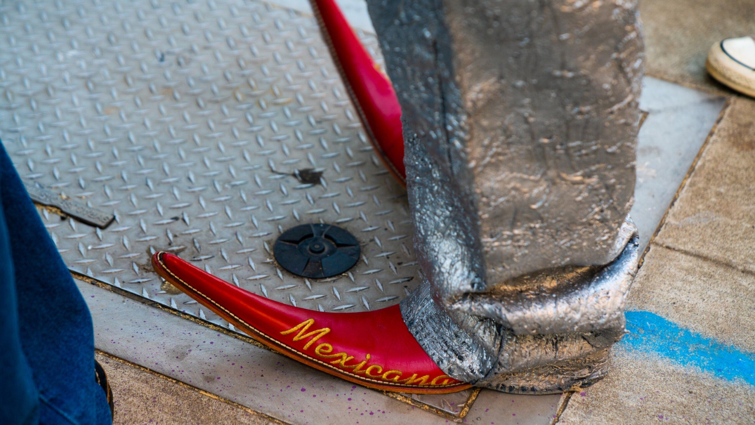 close up of red Botas picudas that say Mexicano on them on city sidewalk.