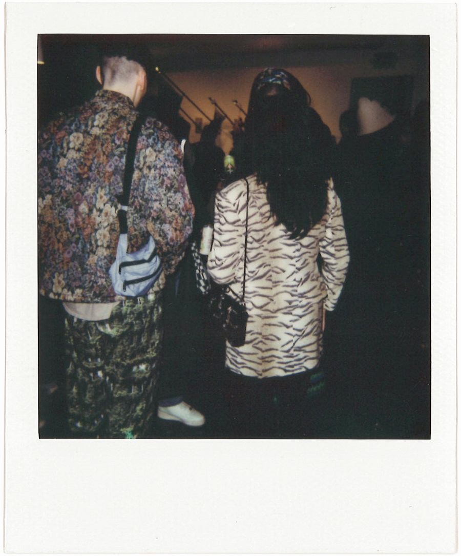 polaroid of the back of two people. one with a colorful jacket and the other with animal print jacket