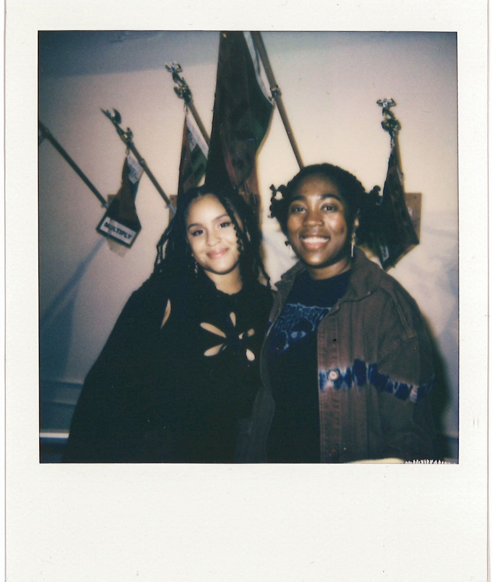 polaroid of two people smiling in front of art flags hanging on wall