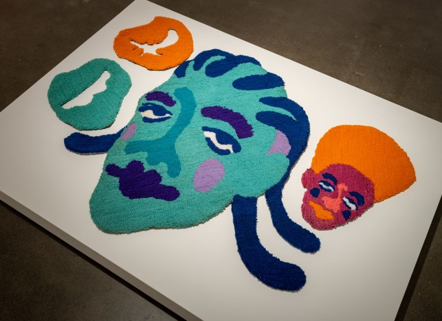 A piece of felt art with a blue, orange, and green face.