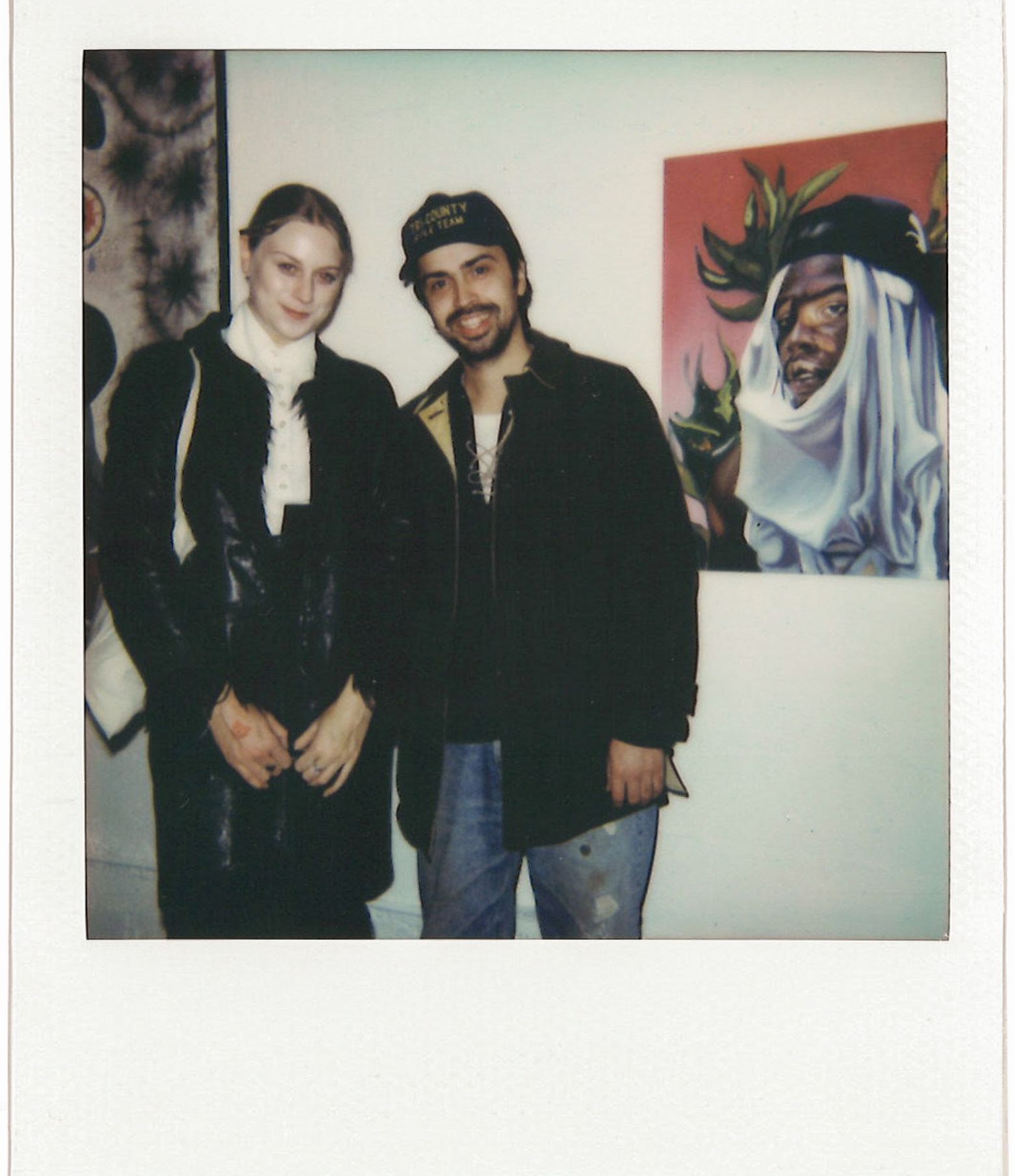 polaroid of two people posing in front of art gallery wall