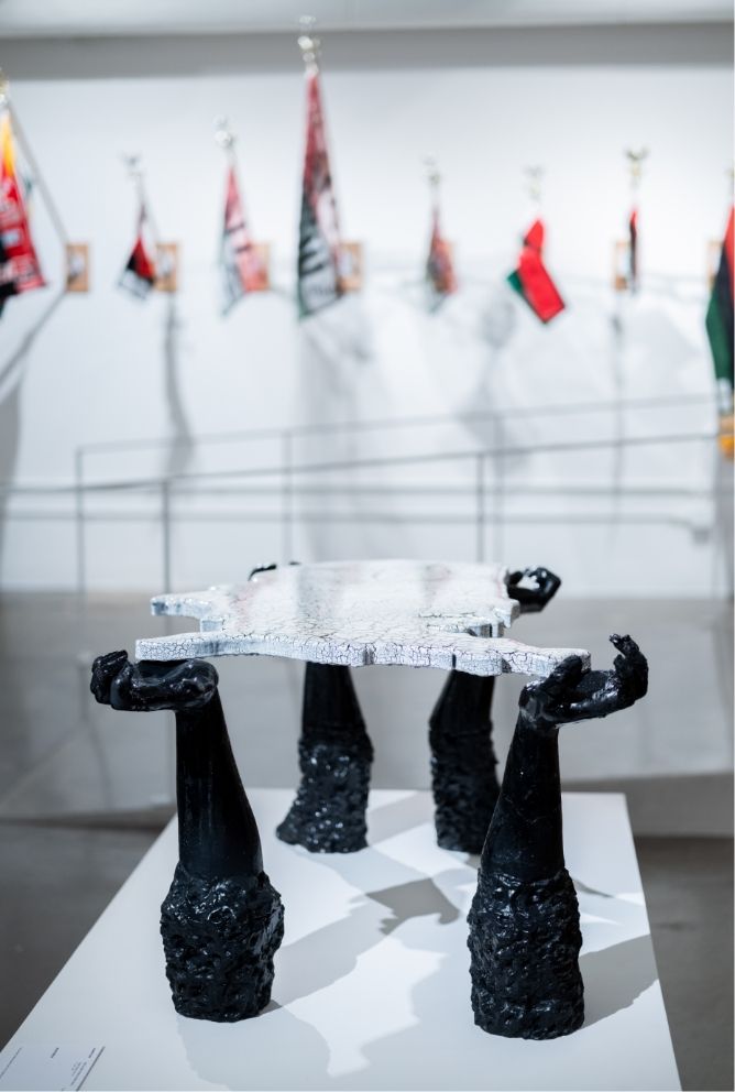 A table comprised of a map of the United States held up by black colored arms and hands