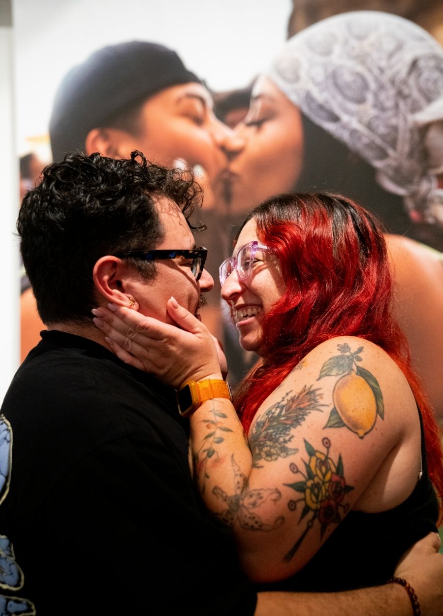 Two people smiling at each other after kissing in front of a large print of two people kissing
