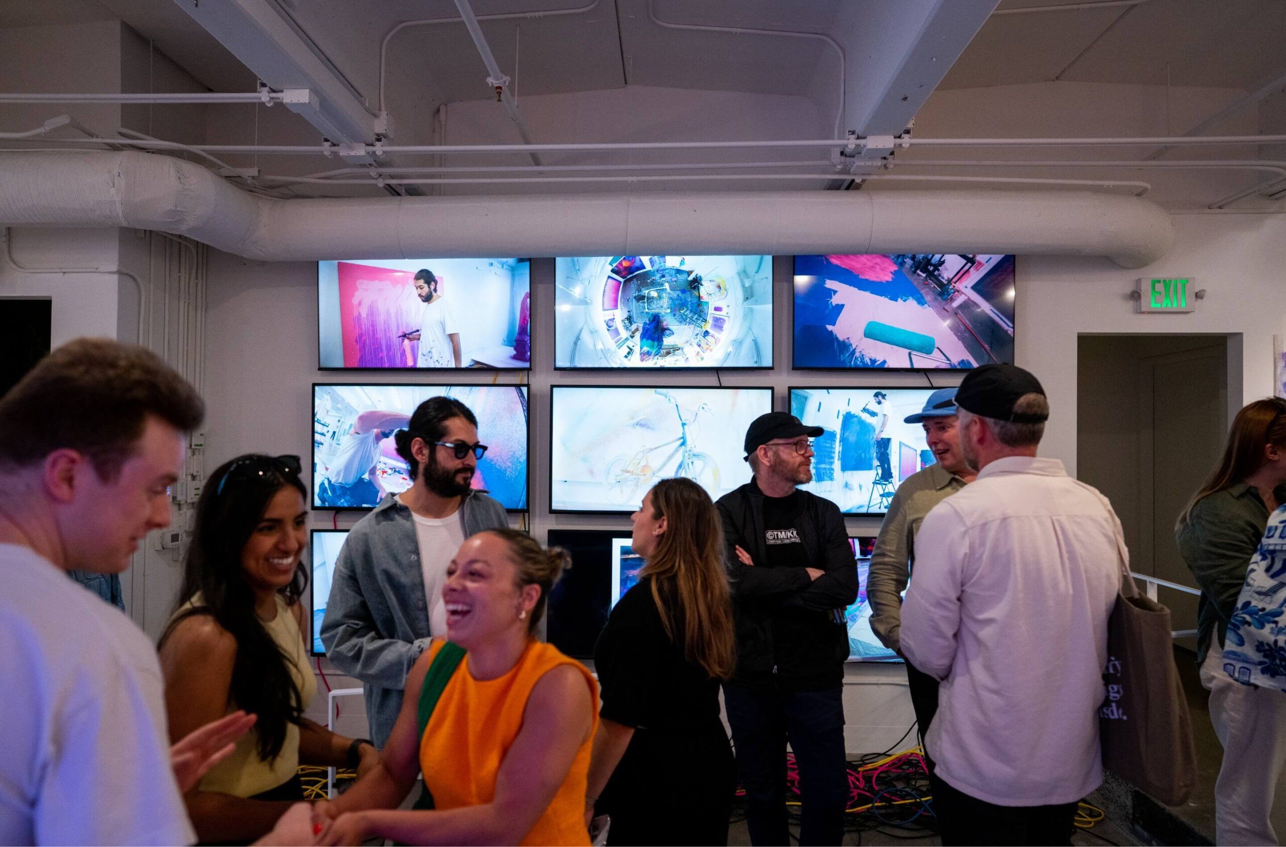 Crowd of people talk in front of video display at exhibit opening
