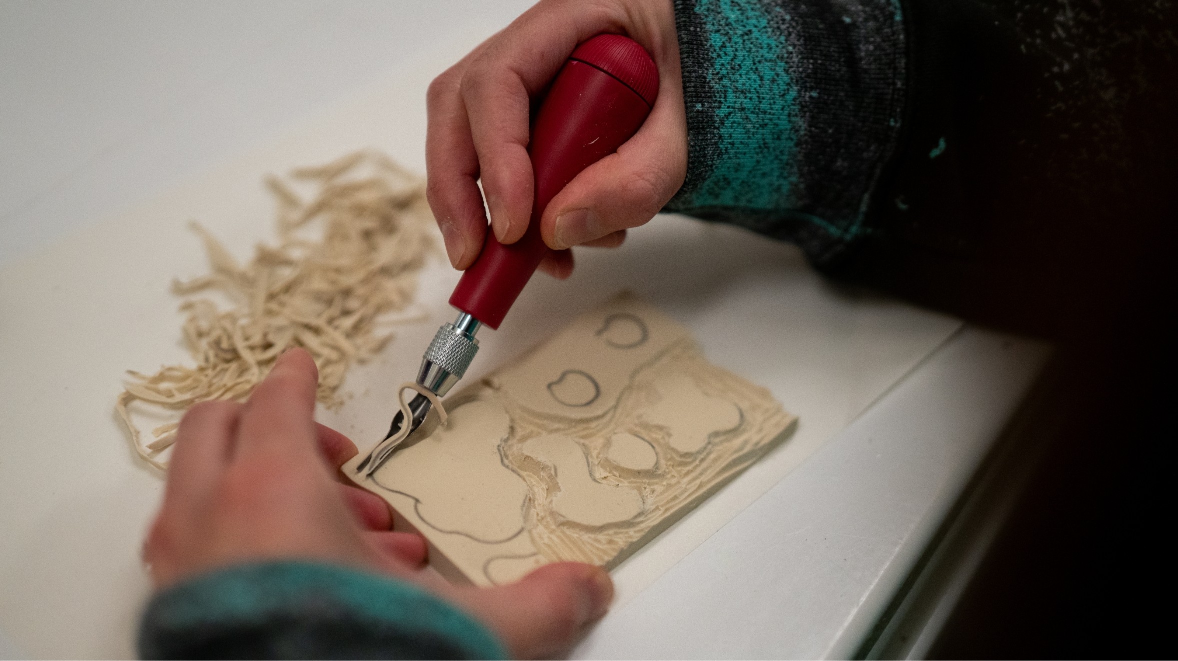 A person cutting a piece of wood with a red tool.