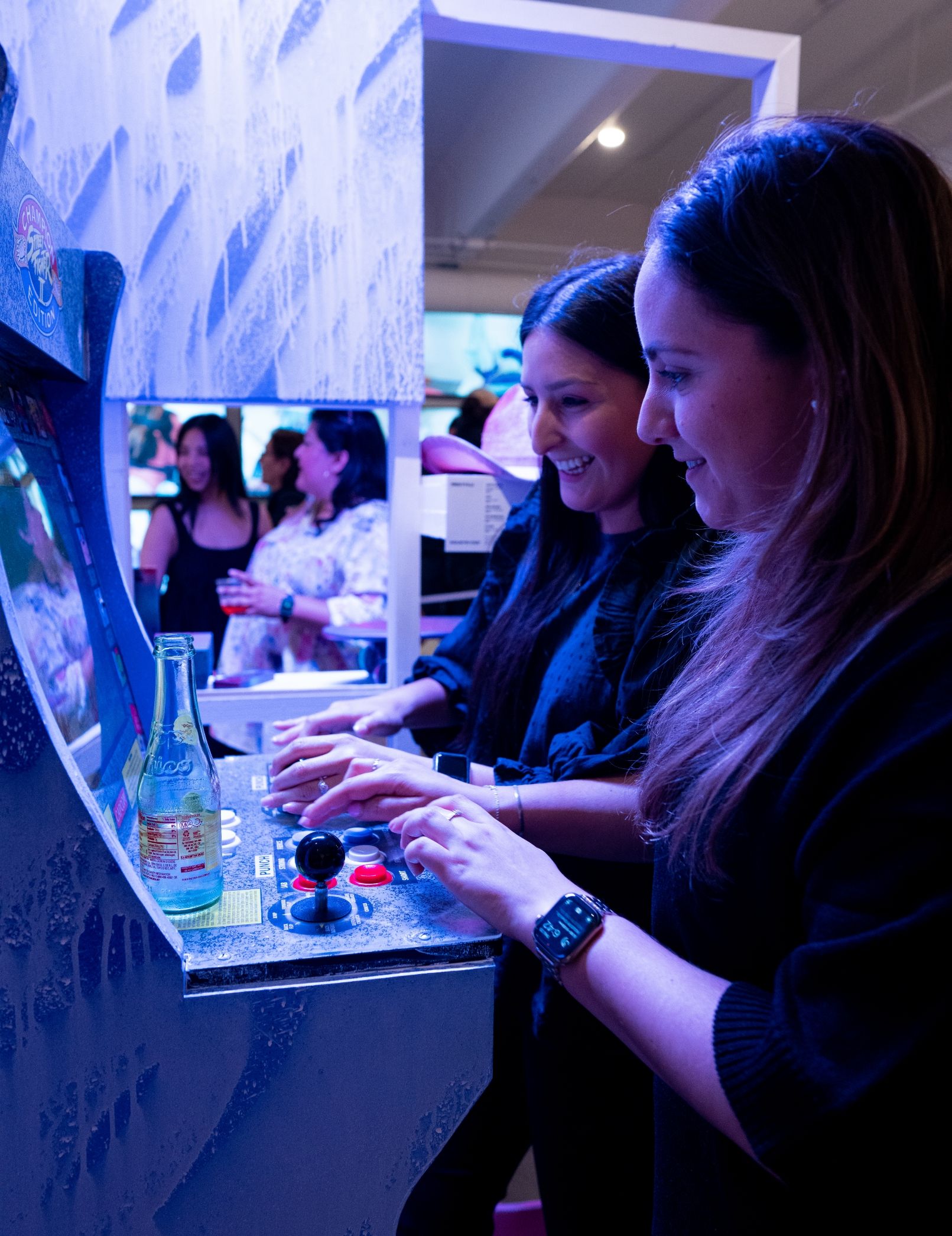 2 people play street fighter 2 arcade game that is spray painted artwork.