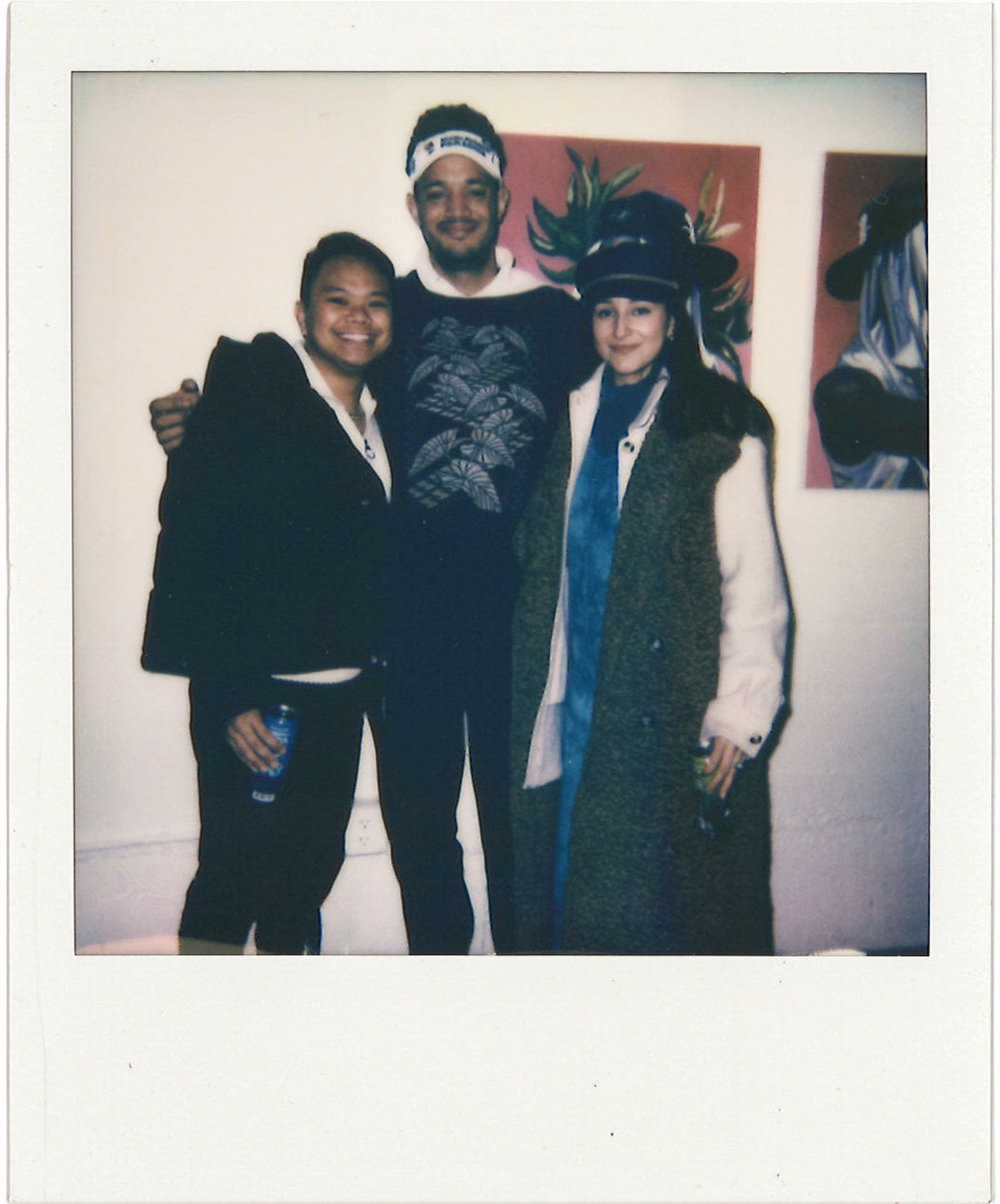 Polaroid of three people with arms around each other and smiling pose in front of art gallery wall
