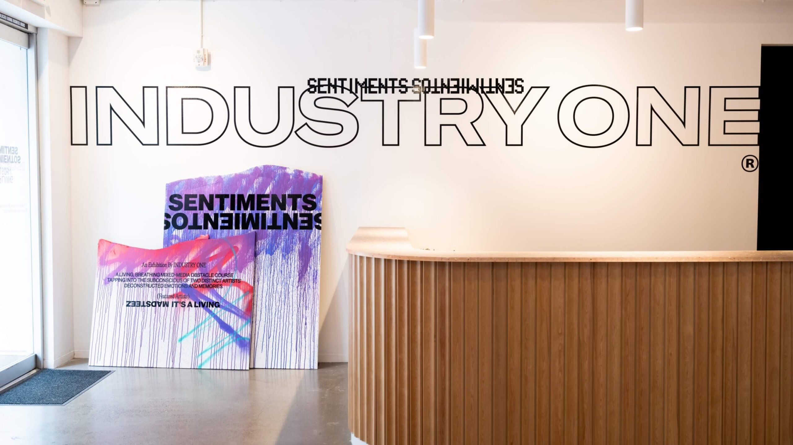 Inside gallery entrance. Vinyl graphics on wall display the words Sentiments Sintimientos Industry One. Spray painted signs also say name of show along with artists names Madsteez and Its a Living